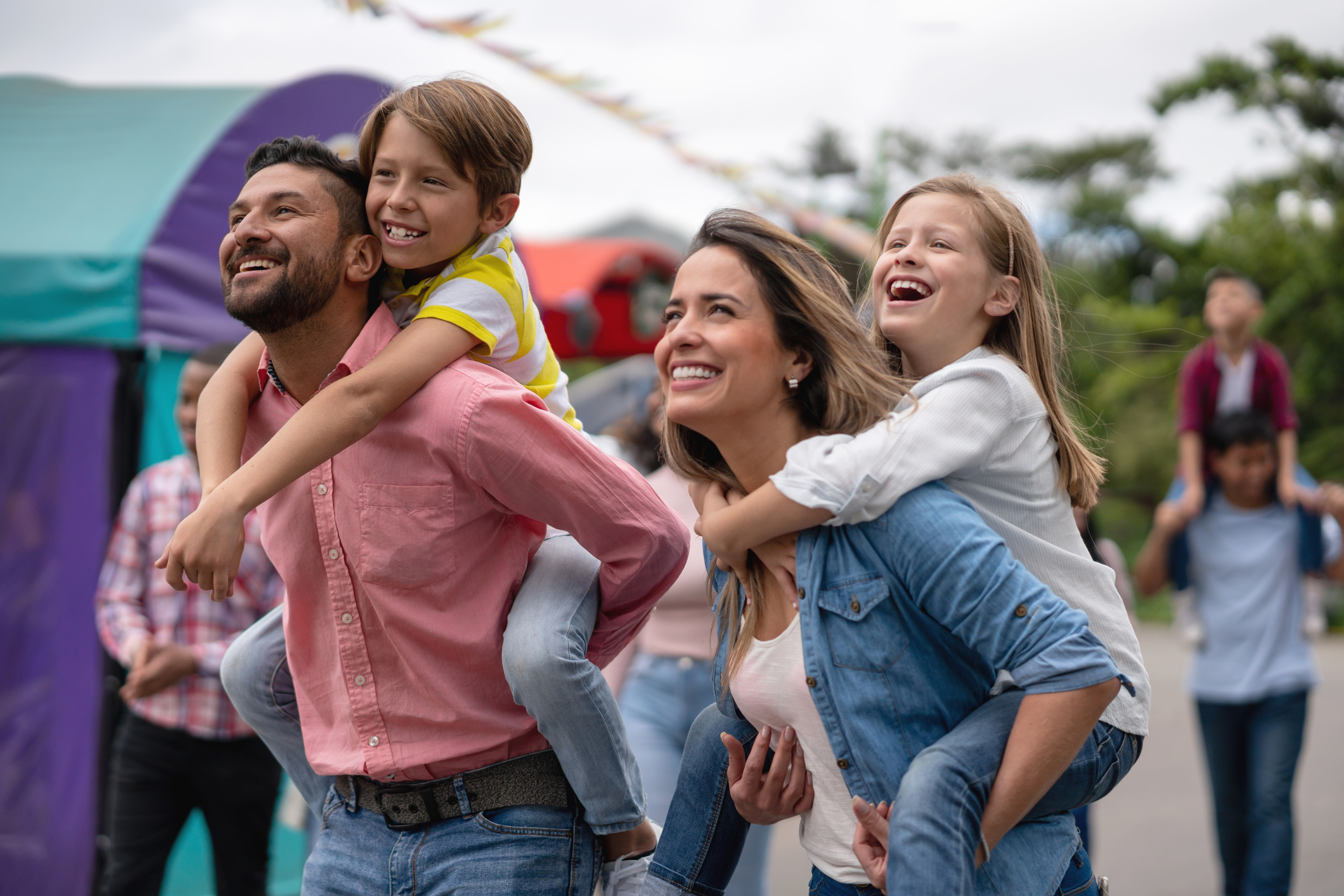 Portrait of a happy family having fun at an amusement park and carrying kids on a piggyback ride 