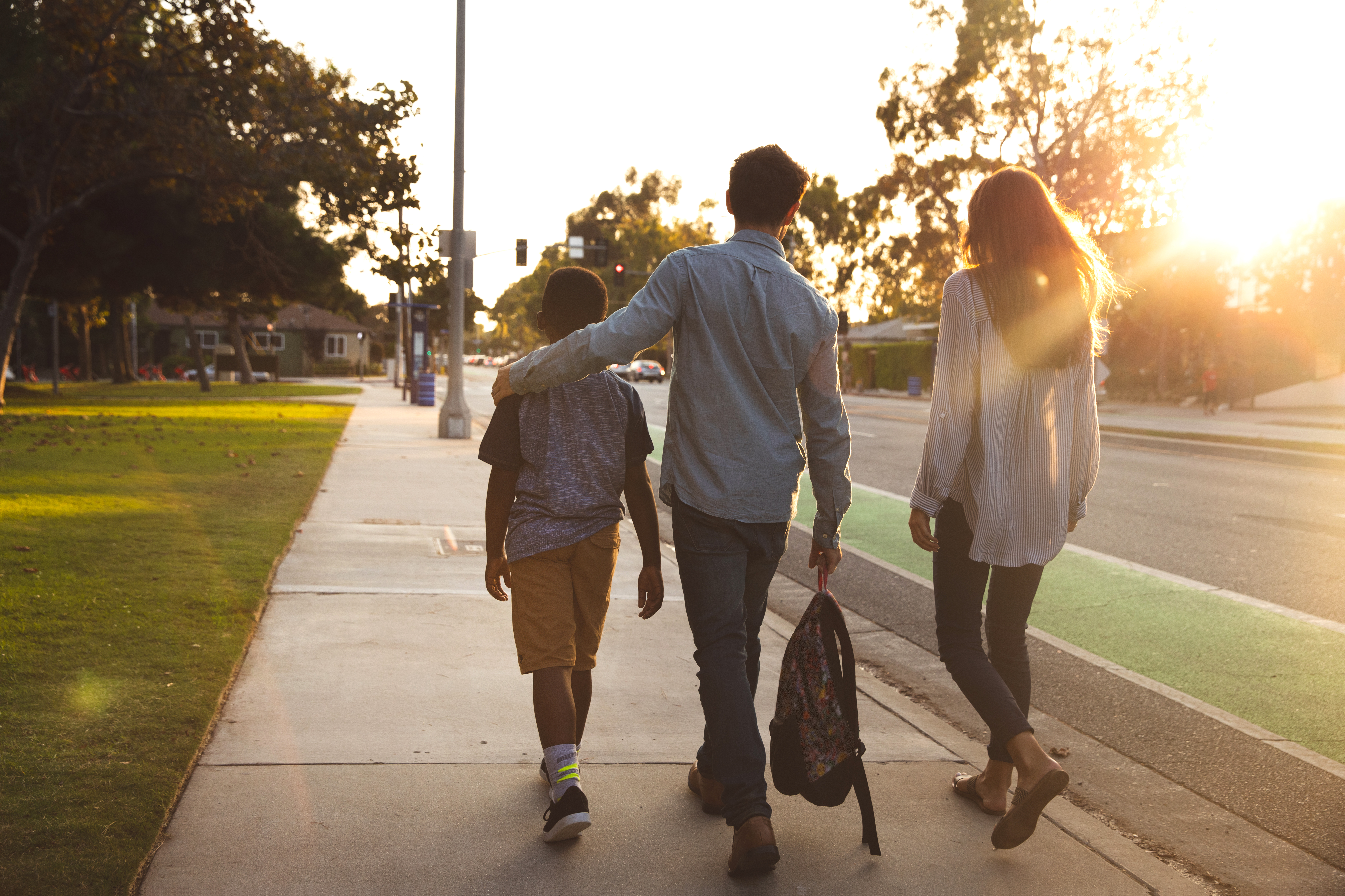 Teen girl and boy walking with a younger boy on the sidewalk.