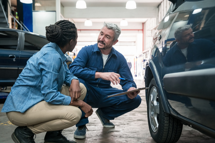 male technician in a vehicle shop explaining details to a woman