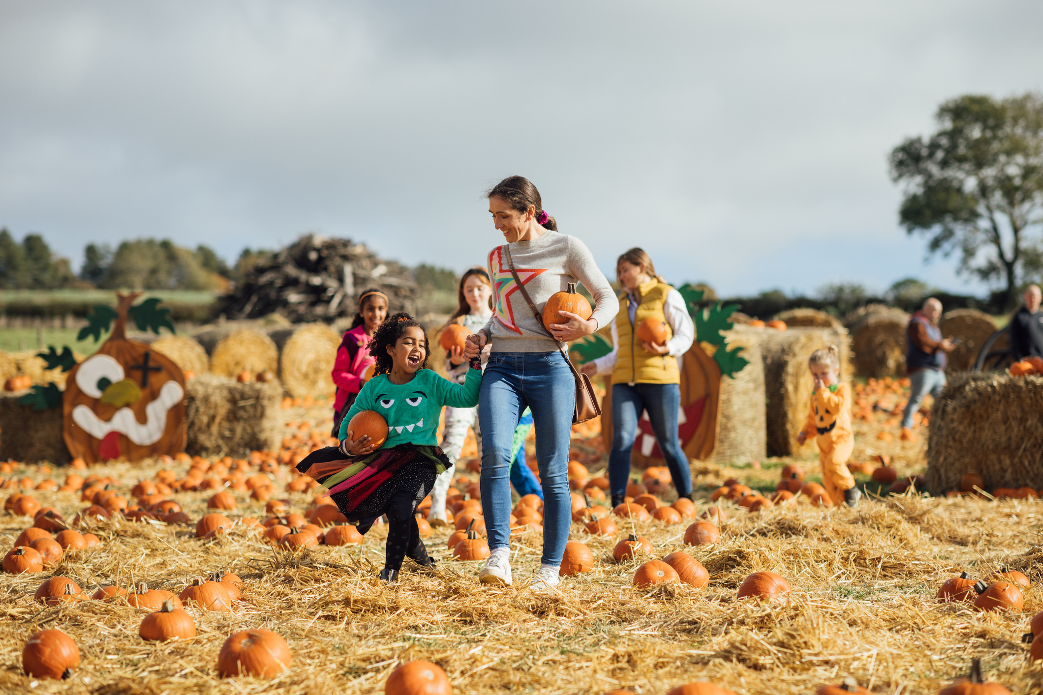  two mothers with their children picking pumpkins for Halloween at a pumpkin patch field